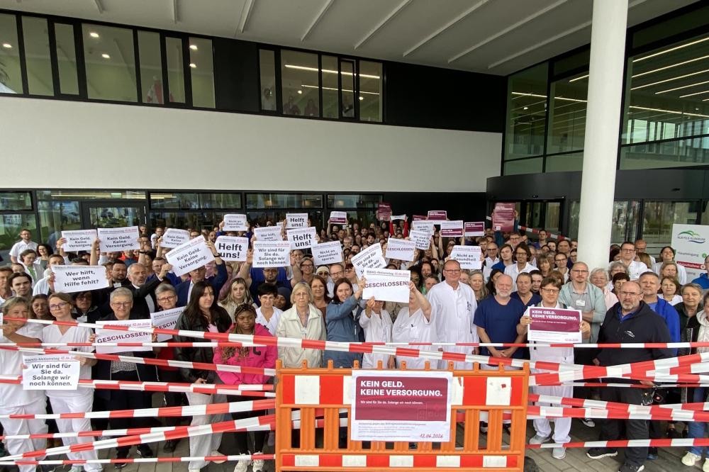 Mitarbeitende halten vor dem Klinik-Haupteingang Protestschilder hoch. Der Bereich ist symbolisch abgesperrt.