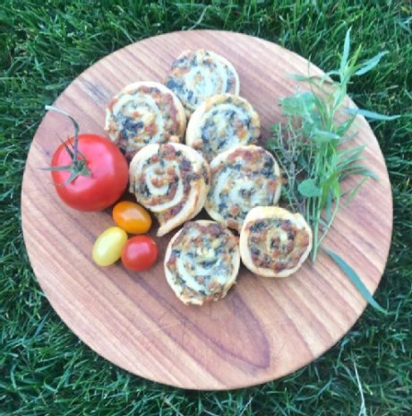 Feta-Spinat-Schnecken auf einem Holzbrett mit Kräuter und Toamten als Deko