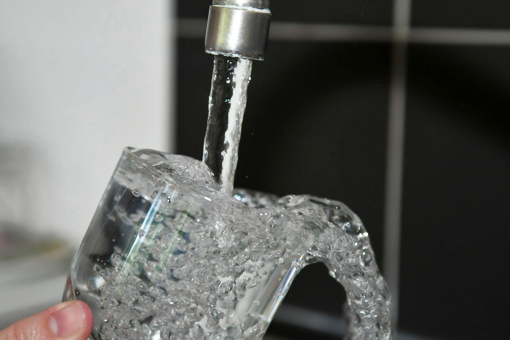 Eine Person hält ein Glas unter einen laufenden Wasserhahn.