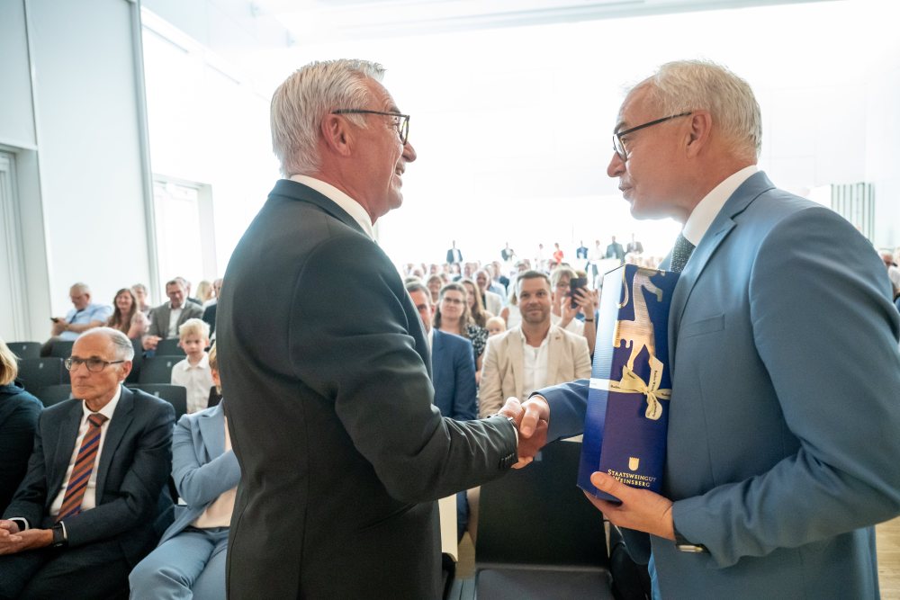 Innenminister Strobl schüttelt stehend Landrat Wolff die Hand. Im Hintergrund sitzt das Publikum.