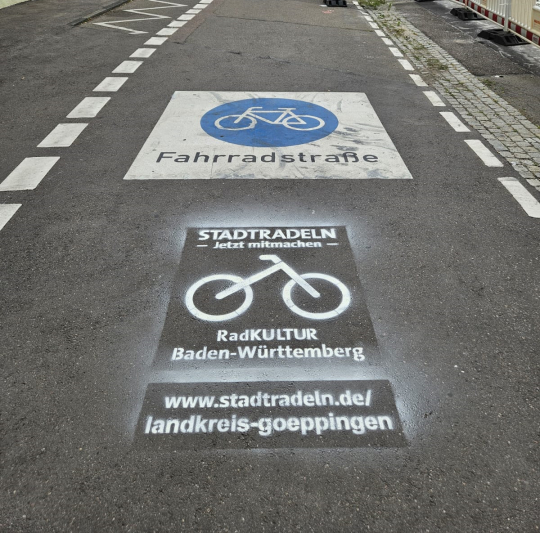 Bild eines blauen Fahrradsymbols auf einer Straße, darunter steht Fahrradstraße, darunter steht auf die Straße gemalt: STADTRADELN, jetzt mitmachen