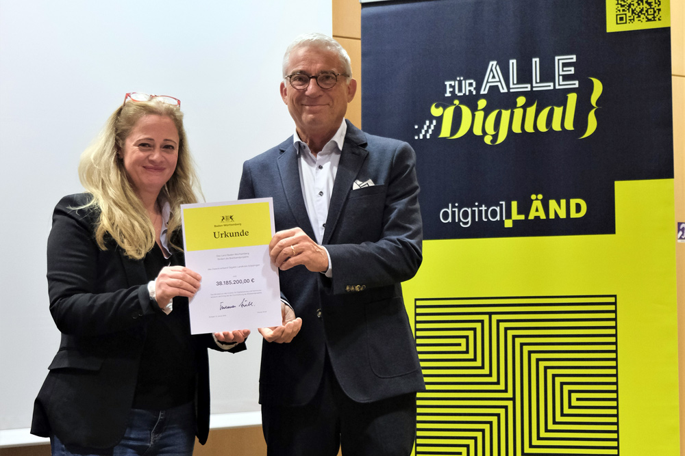 Thomas Strobl und Tülin Gömec schauen in die Kamera und halten eine Urkunde ins Bild.