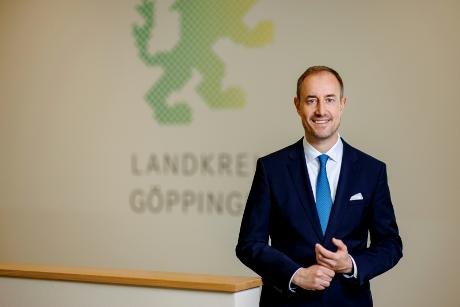 Landrat Markus Möller steht vor einer Wand, auf der das Signet des Landkreises erkennbar ist (ein grüner Löwe).