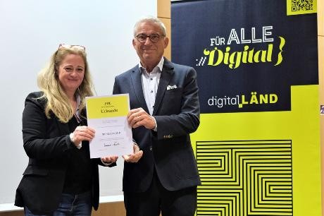 Übergabe des Förderbescheids Thomas Strobl und Tülin Gömec schauen in die Kamera und halten eine Urkunde ins Bild.