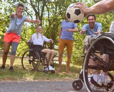 Gruppenbild mit 2 Rollstuhlfahrern und weiteren Personen, die Ball spielen