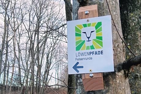Löwenpfad-Felsenrunde Wanderzeichenschild im Wald mit einem Löwenkopf-Symbol.