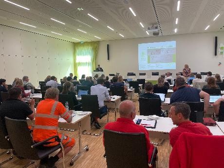 Auf dem Foto sind die Teilnehmenden der Tagung zu sehen. Sie sitzen im Sitzungssaal und hören einem Vortrag interessiert zu. 