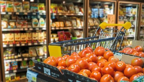 Einkaufswagen in einem Supermarkt, daneben eine Kiste mit Tomaten